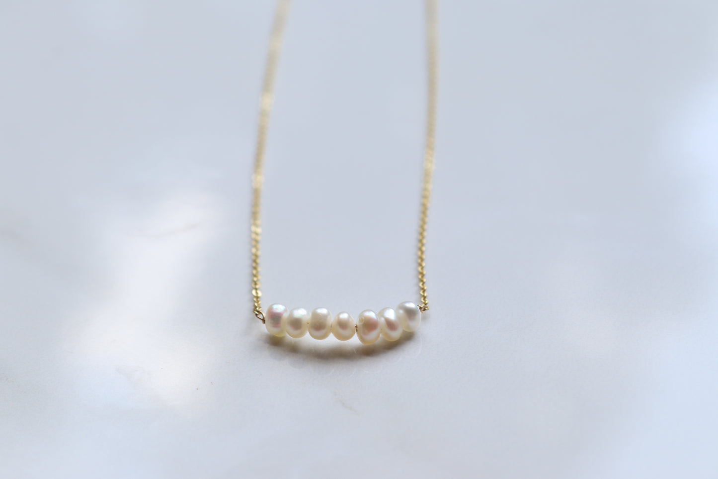 Pearl necklace on a thin gold chain against a light background