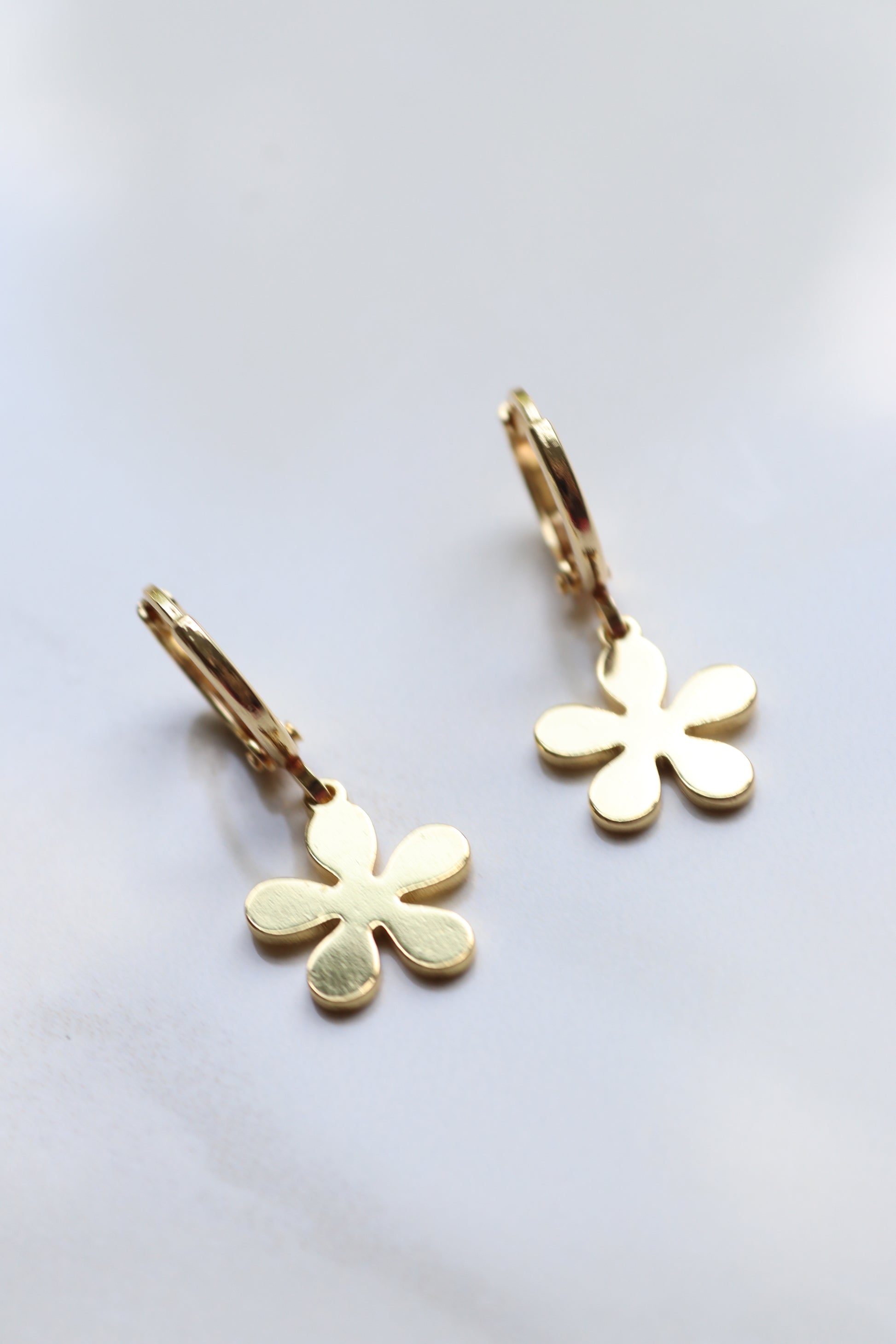 Gold flower-shaped earrings on a light gray background