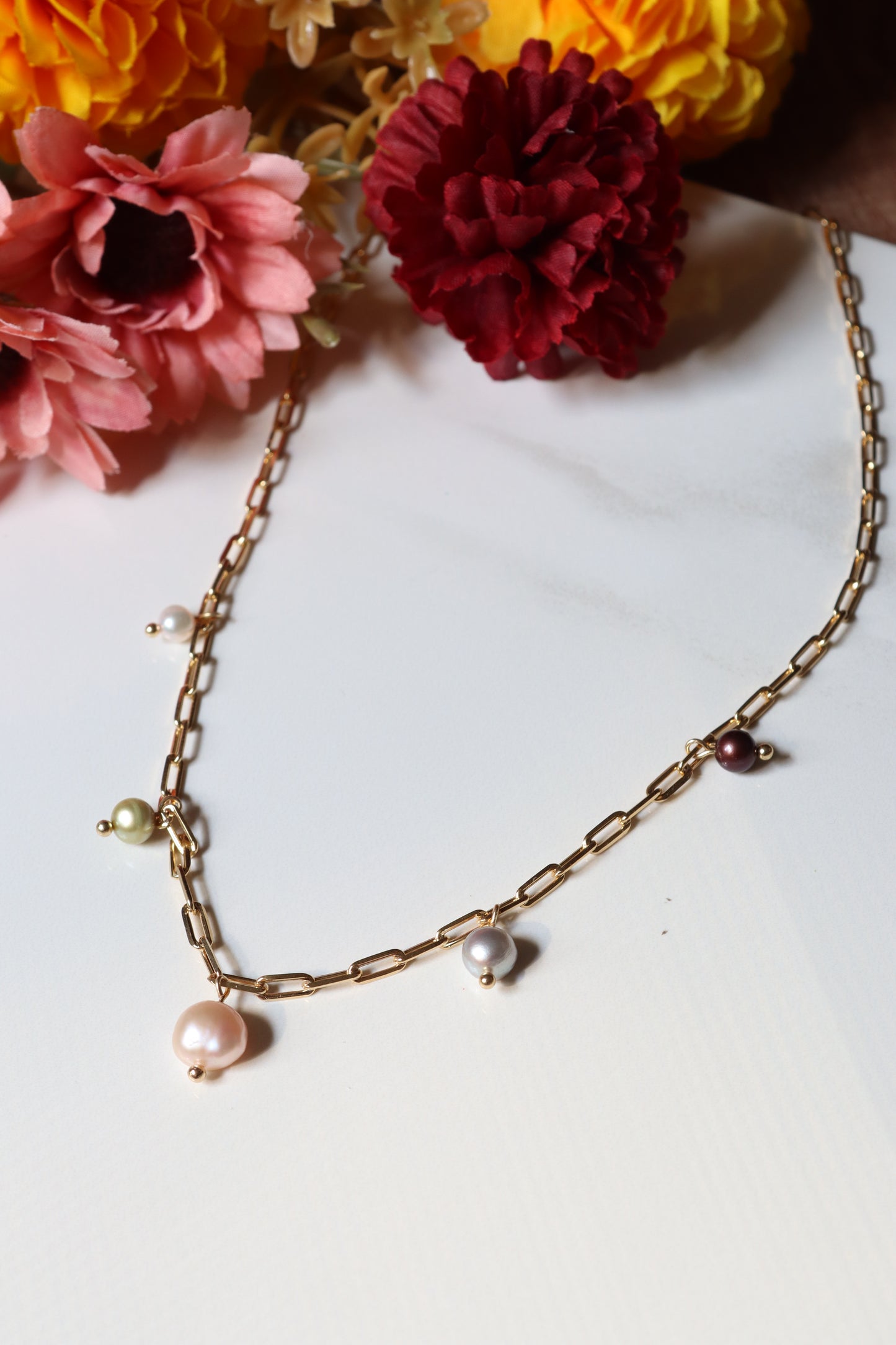 Gold chain necklace with pearls on a white background with flowers