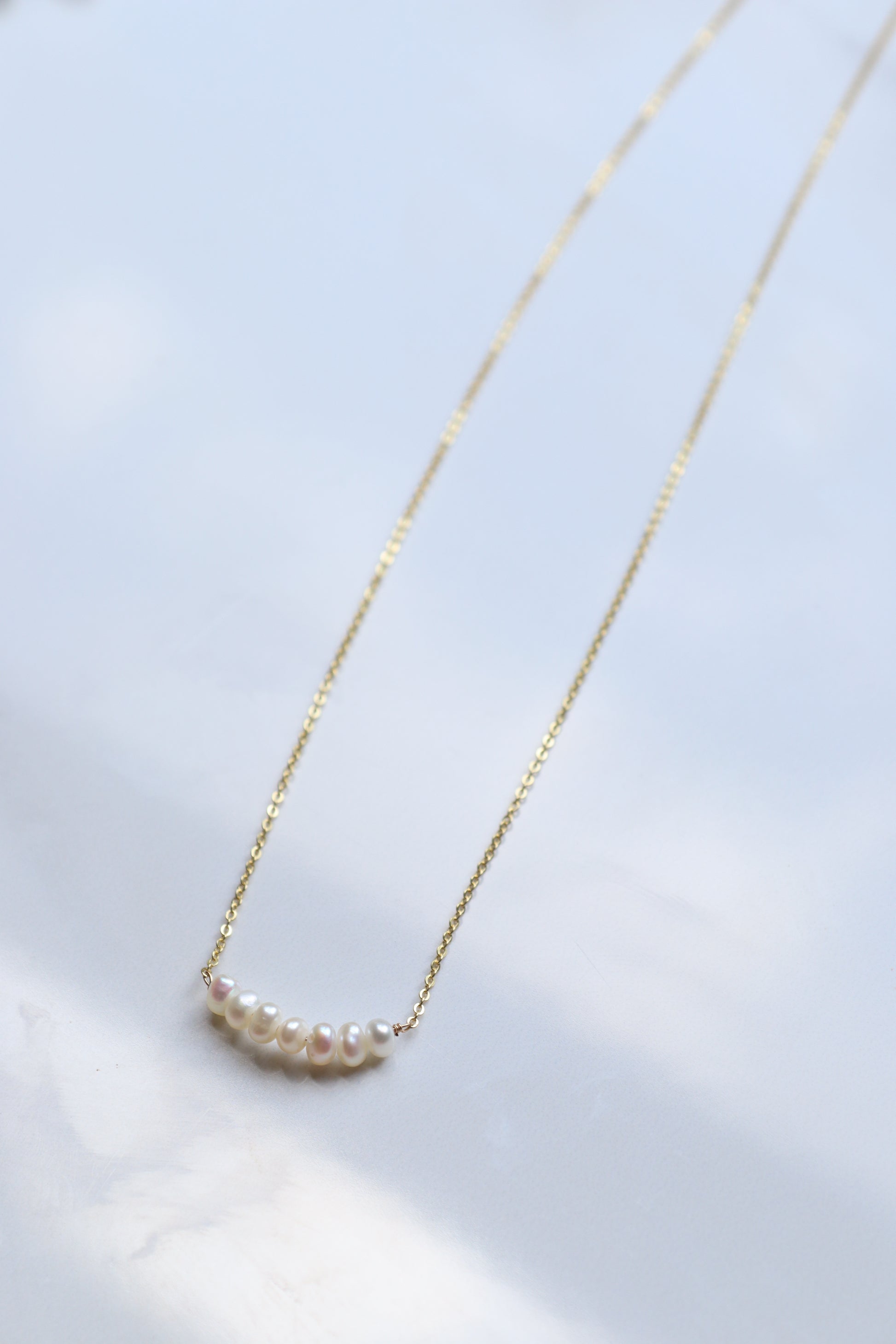 Gold necklace with a small pearl pendant on a light background